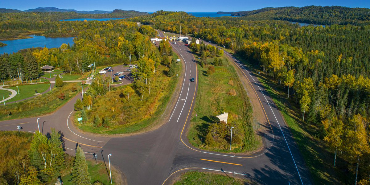 aerial view of highway lined with forest, rocks, and lakes